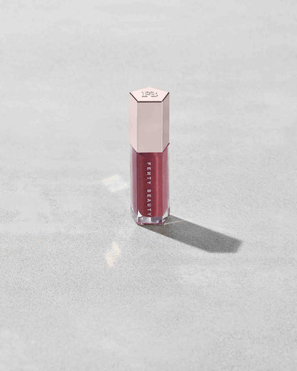 A closed tube of Gloss Bomb Universal Lip Luminizer in the shade RiRi on a grey background.