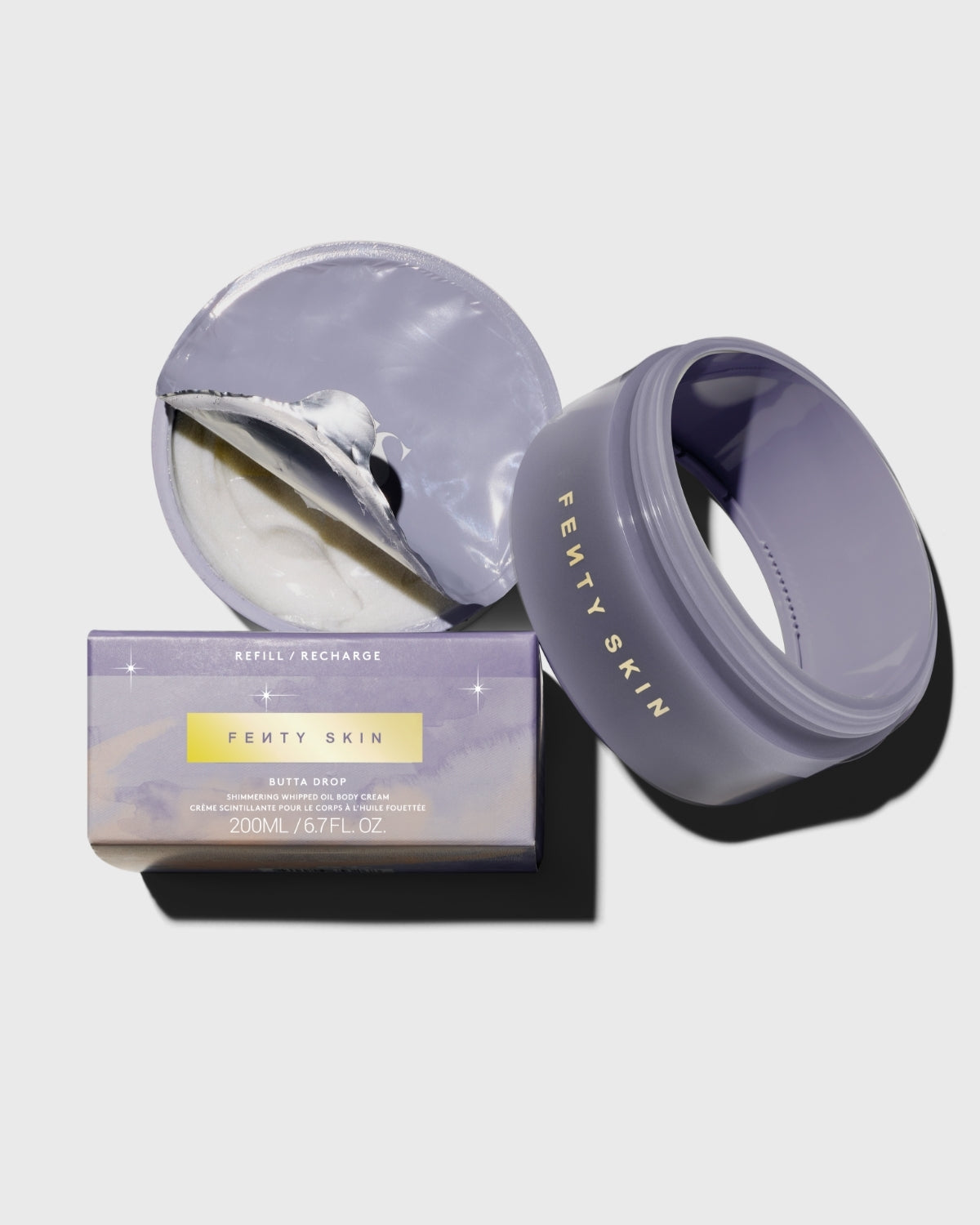 Product shot of Butta Drop Shimmering Whipped Body Oil and packaging on a lavender background.